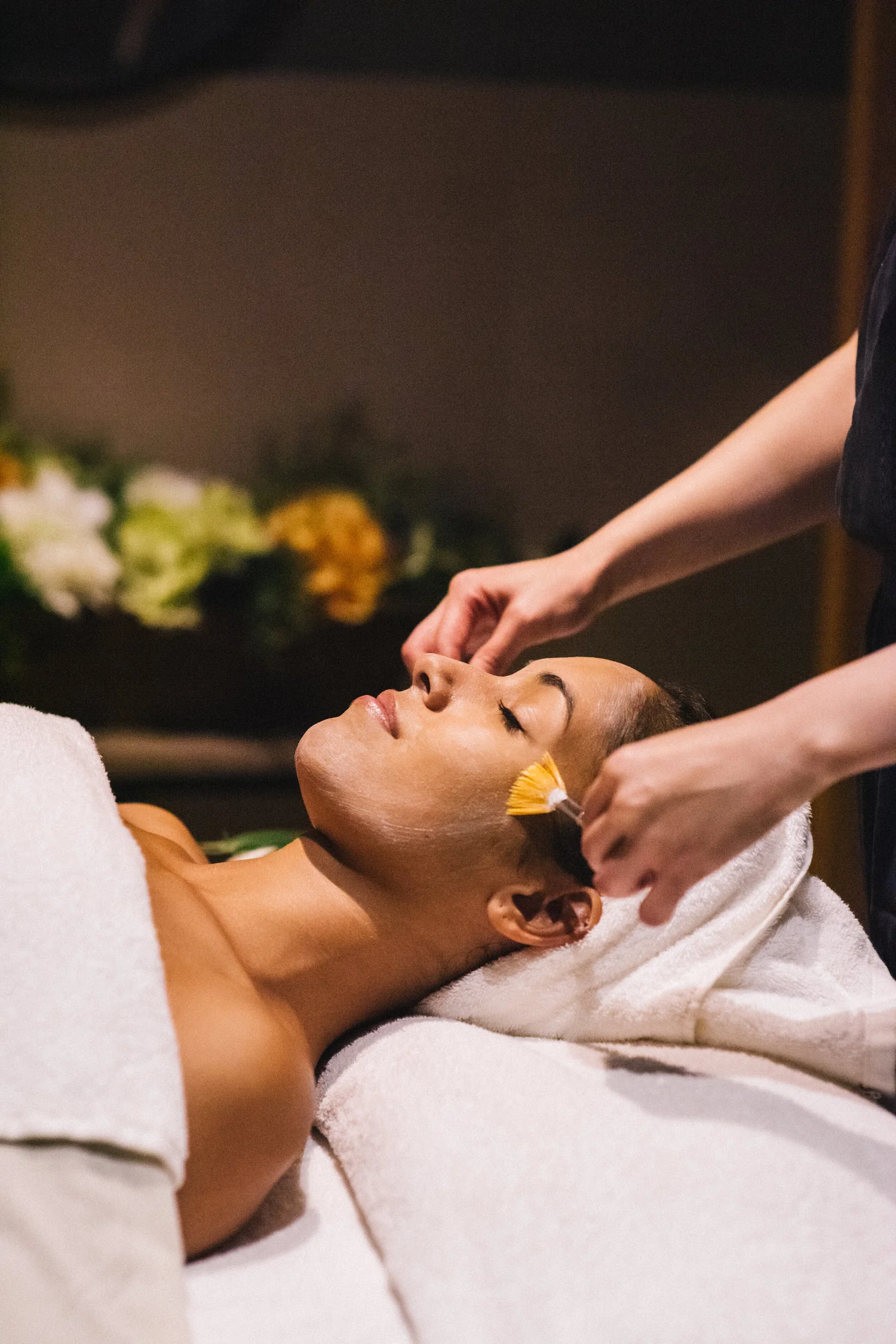 Client reclining while an esthetician applies product with a facial brush