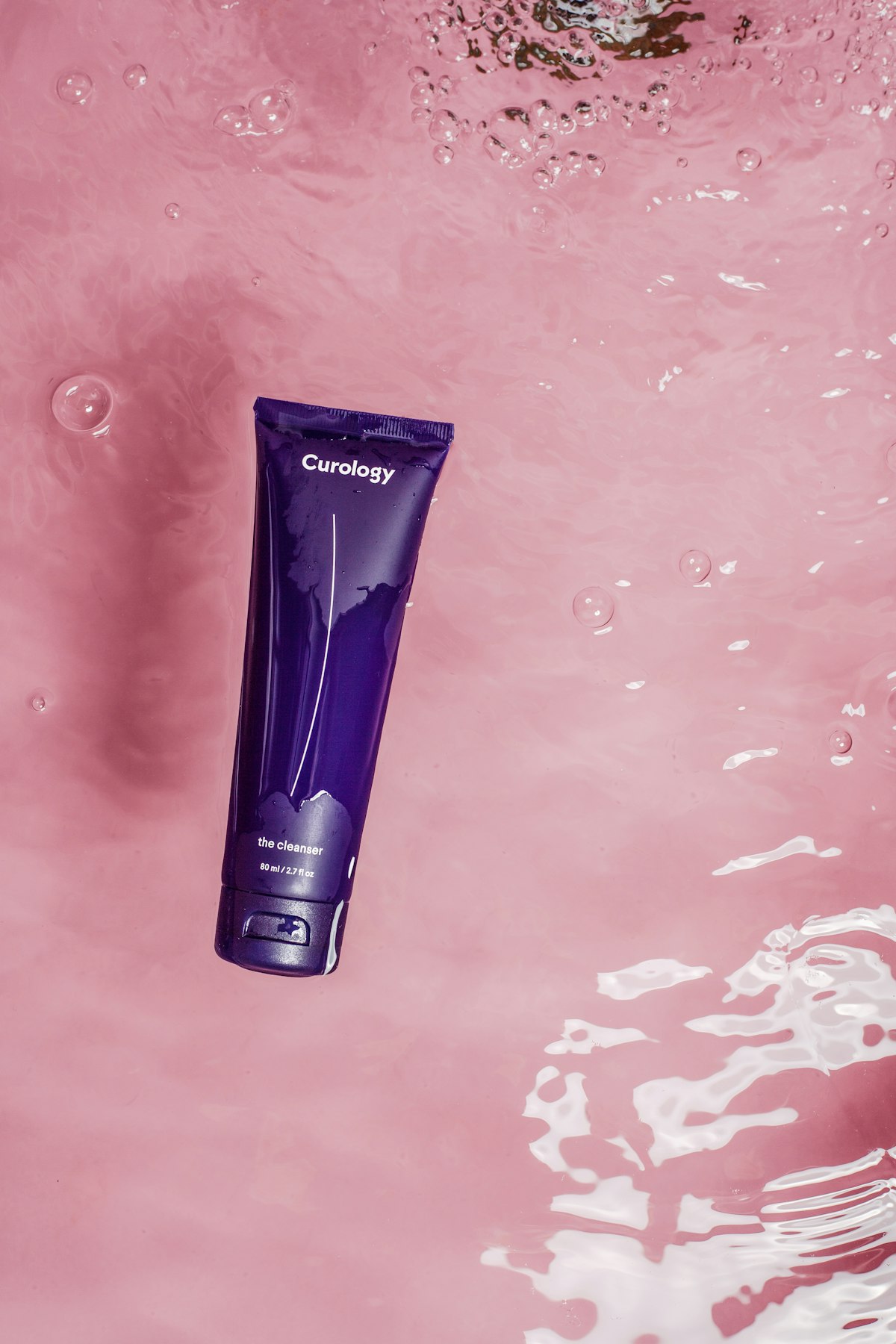 Skincare tube on a pink textured surface